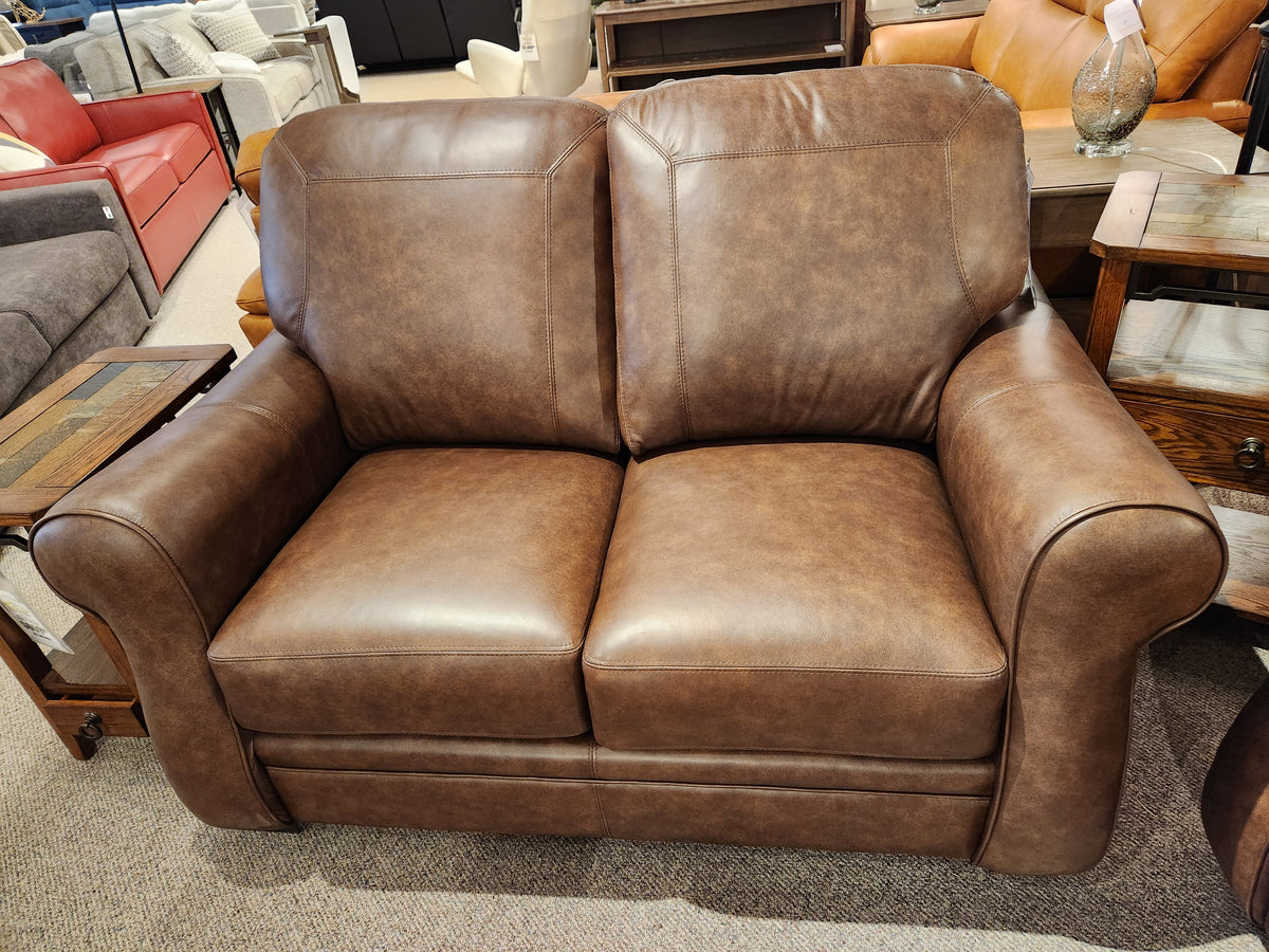 The Orangeville Leather Loveseat by Leather Craft features rolled arms and cushions, displayed in a Toronto showroom.