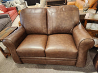 The Orangeville Leather Loveseat by Leather Craft features rolled arms and cushions, displayed in a Toronto showroom.