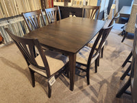 The showroom features a rustic Handstone Parker 7pc Dining Package with a dark wood table and six cushioned chairs.