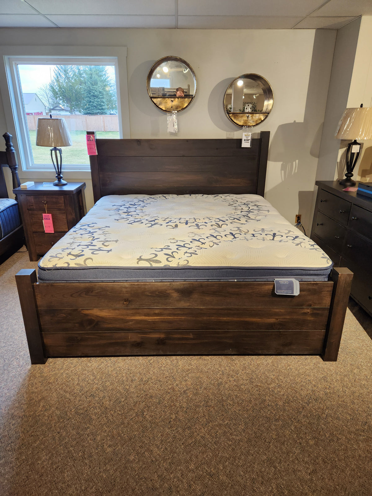 Wooden bed with a Stearns & Foster Mon Amour Euro-Top Firm Mattress, side tables, and mirrors on display.