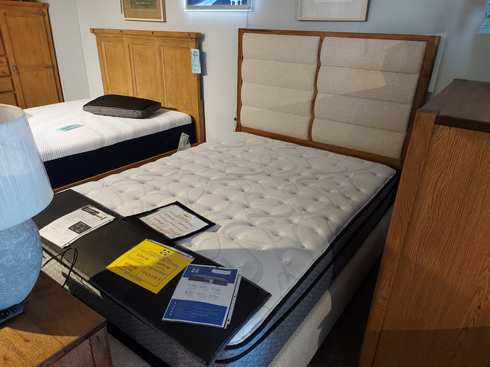 A showroom showcases Vaughan Bassett's 790 Erin's Queen Bed with a solid oak frame, quilted mattress, brochures, and a pillow.