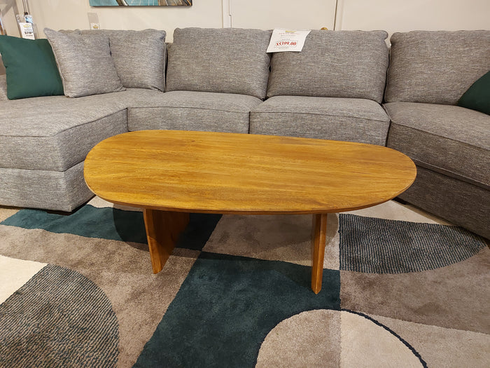 Crestview Collection Ashland Cocktail Table in natural mango wood sits on a patterned rug before a gray sectional with green pillows.