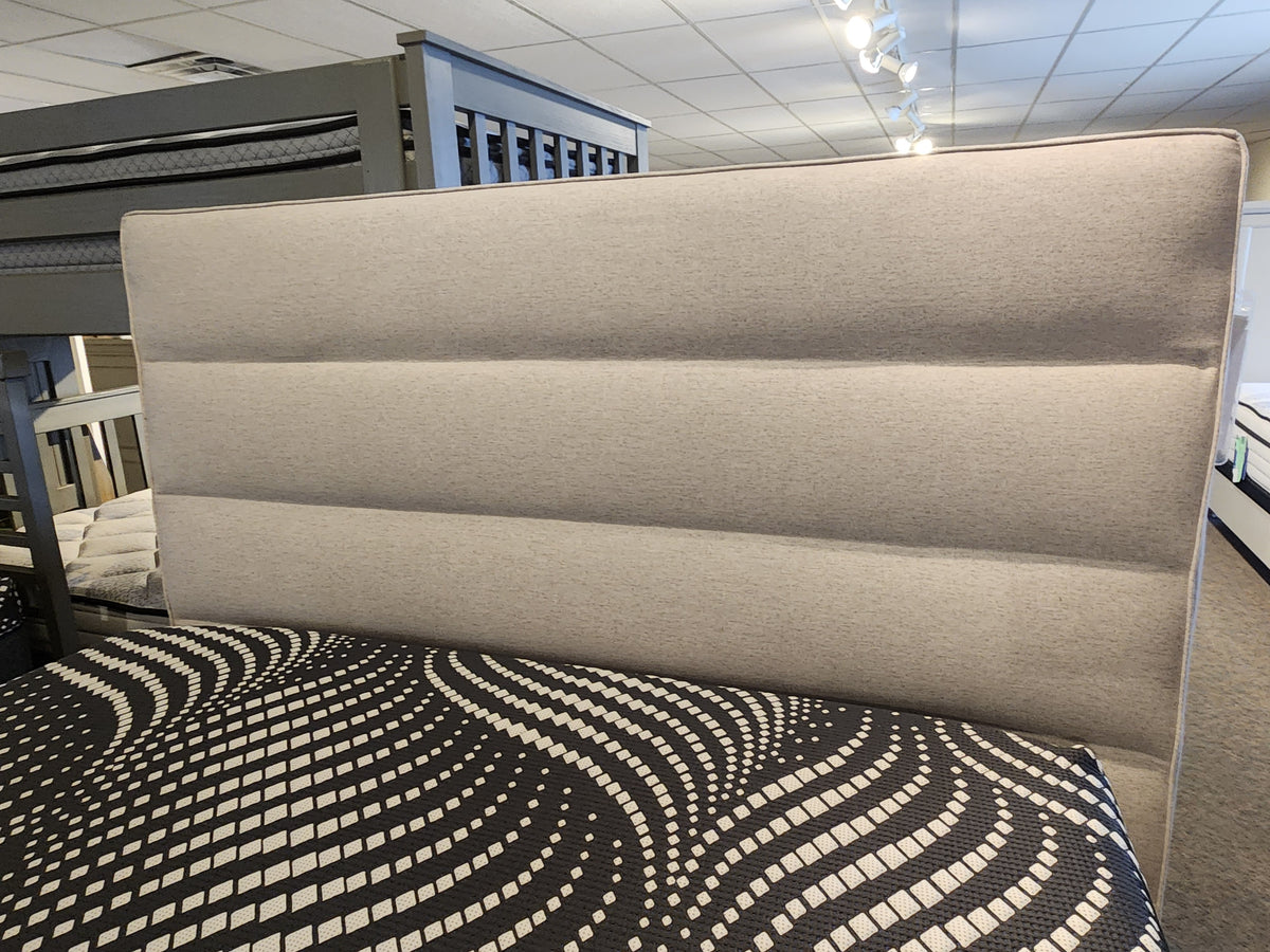 The Julien Beaudoin Queen Adelaide Upholstered Bedframe with a patterned mattress is showcased in a modern showroom.