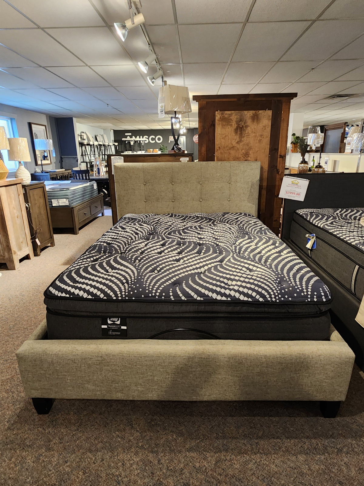 The Queen Heaven Upholstered Bedframe by Julien Beaudoin with a tufted headboard is displayed among wooden furniture.