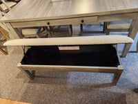 The Ashley D291 Parellen Upholstered Storage Bench in gray sits open in front of the dining table.