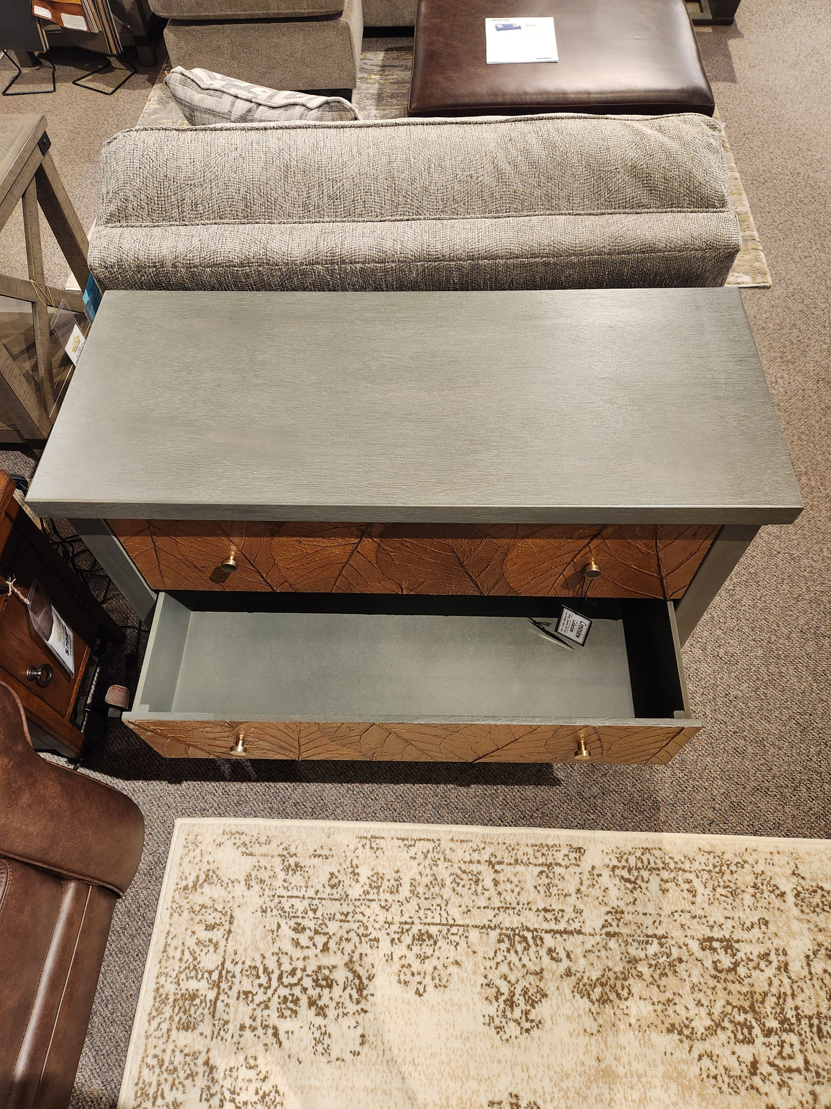 The Crestview Collection Arbor Three Drawer Chest, in gray with natural wood drawers, on display in a showroom.