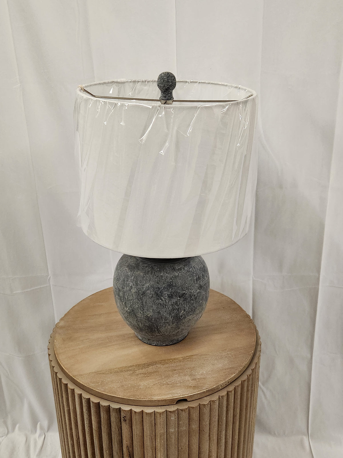 The 862D0 Anza Table Lamp by Pacific Coast, with a drum shade, is displayed on a wooden pedestal against a white backdrop.