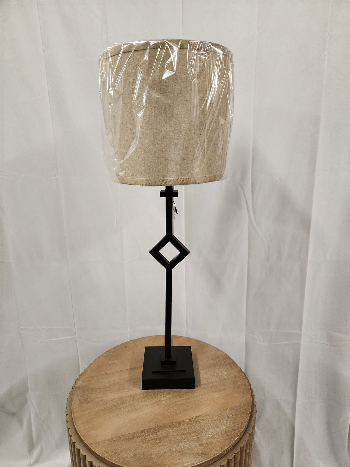 The Pacific Coast 519V0 Audrey Table Lamp with a neutral drum shade sits on a round wooden table.