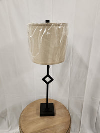 The Pacific Coast 519V0 Audrey Table Lamp with a neutral drum shade sits on a round wooden table against a white backdrop.