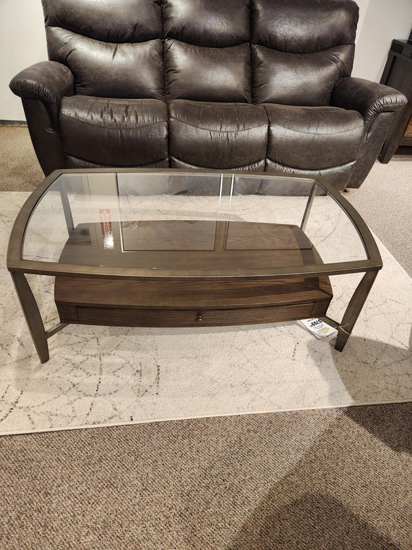 The Magnussen T5692 Ardis Coffee Table features a glass top, oak veneer frame, and lower shelf on a light rug.