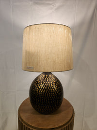 The Ashley Maire Table Lamp has a black and goldtone round base and beige shade for urban industrial style.