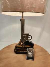 Quick Draw Table Lamp with a tall gun-themed base, round shade, by Crestview Collection on a wood surface.