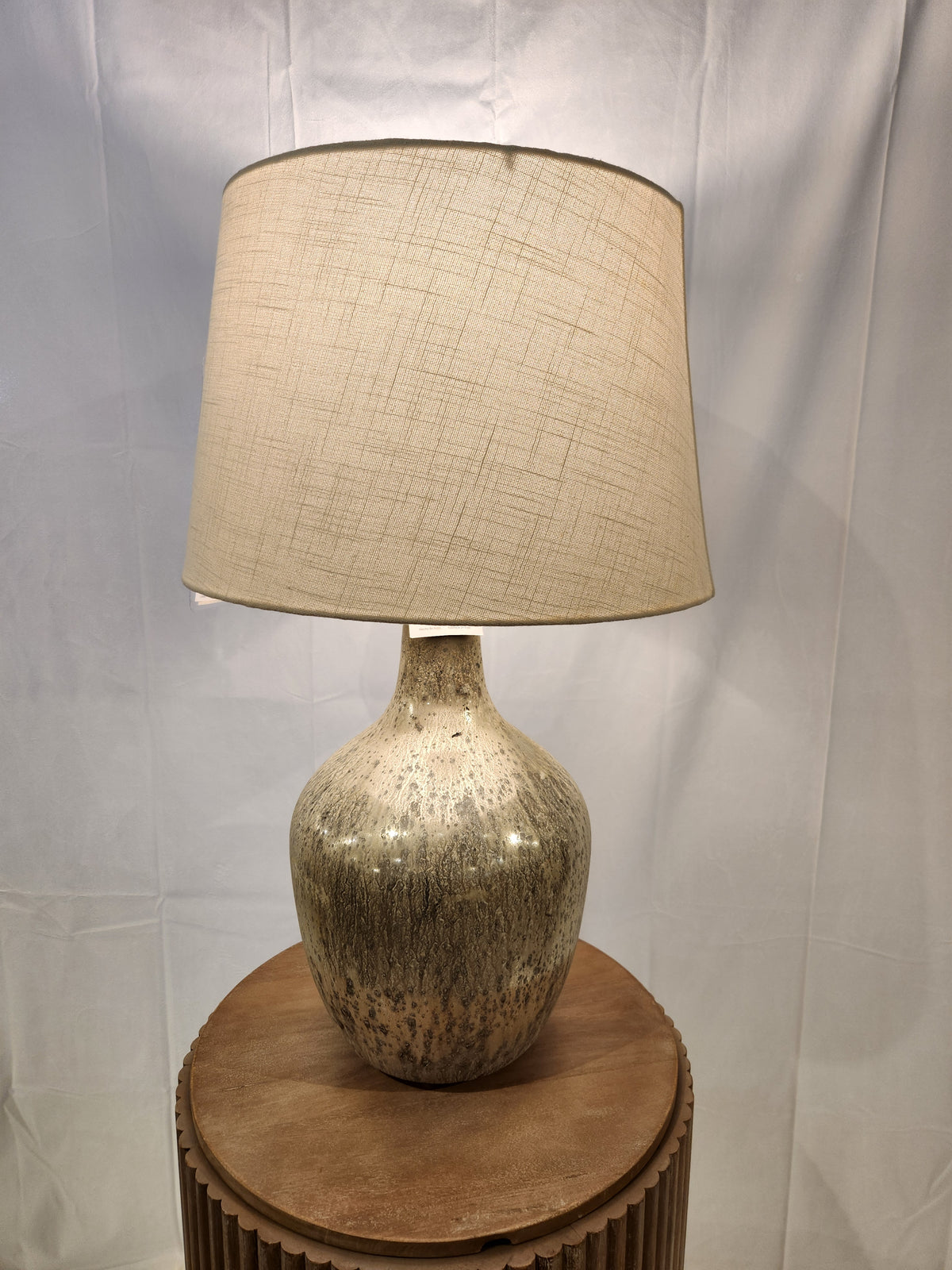 The Ashley Mari Table Lamp with a textured beige shade radiates vintage vibes on a round wooden table.