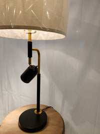 The 96J17 Holmes Table Lamp by Pacific Coast with a black and brass base sits on a round wooden table.