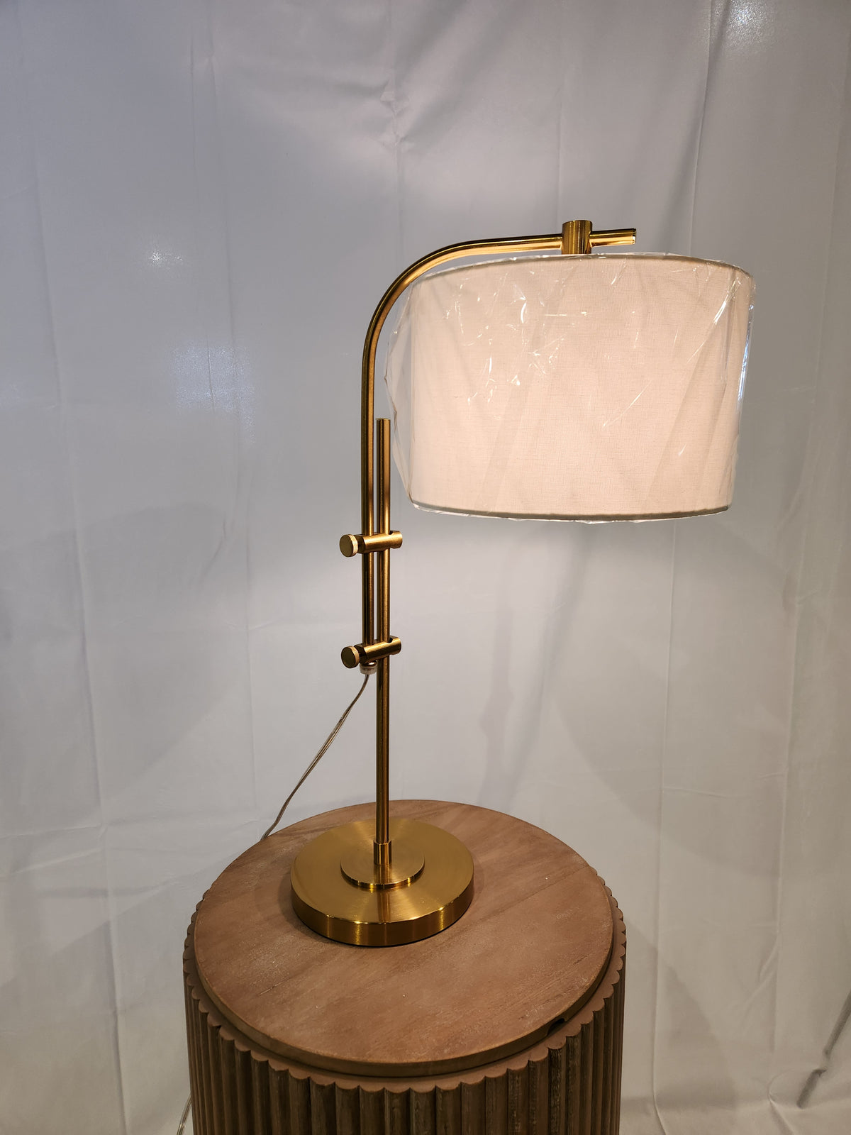 An Ashley Baronvale L206053 Table Lamp with a brass-tone finish and white shade sits on a round wooden table.