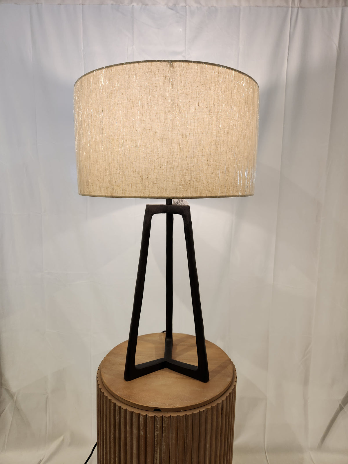 An Ashley Ryandale Table Lamp with a fabric shade and antiqued black finish sits on a round wooden table.