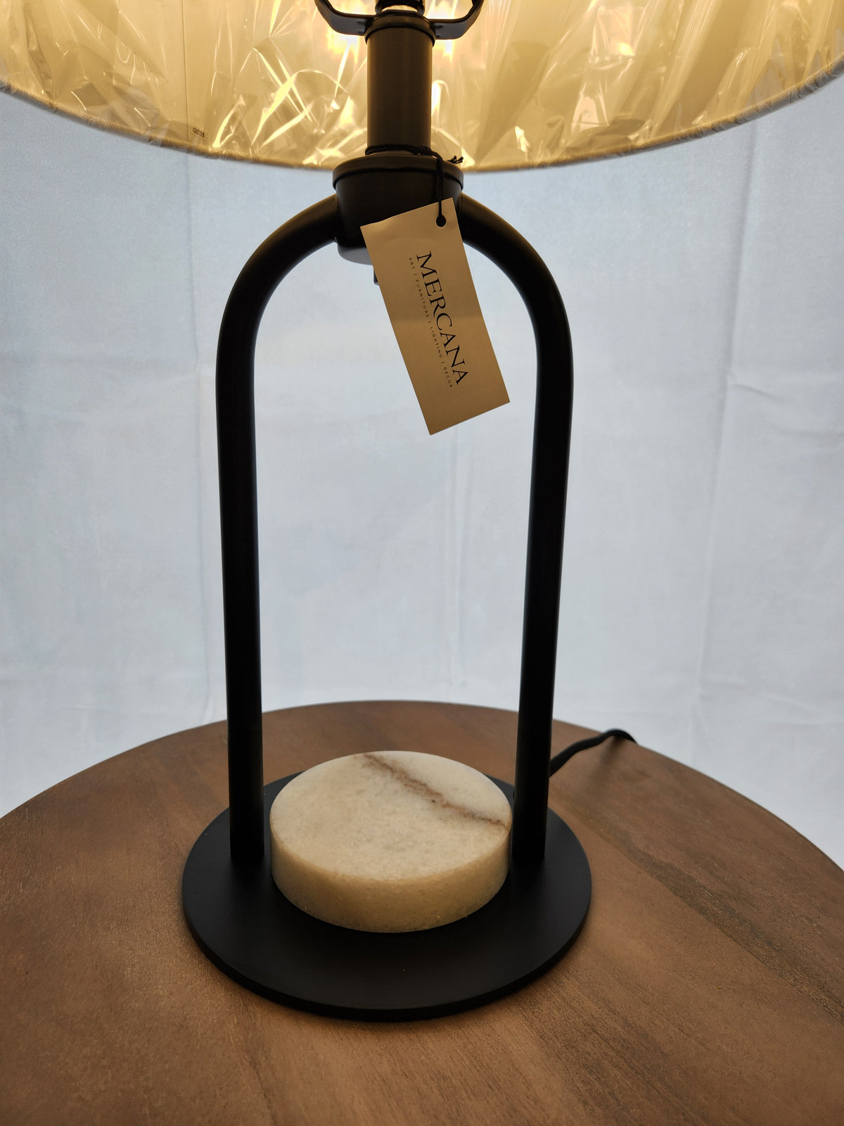 The Mercana 69702 Sarah Table Lamp features a black arched metal frame and white marble disc base on wood.