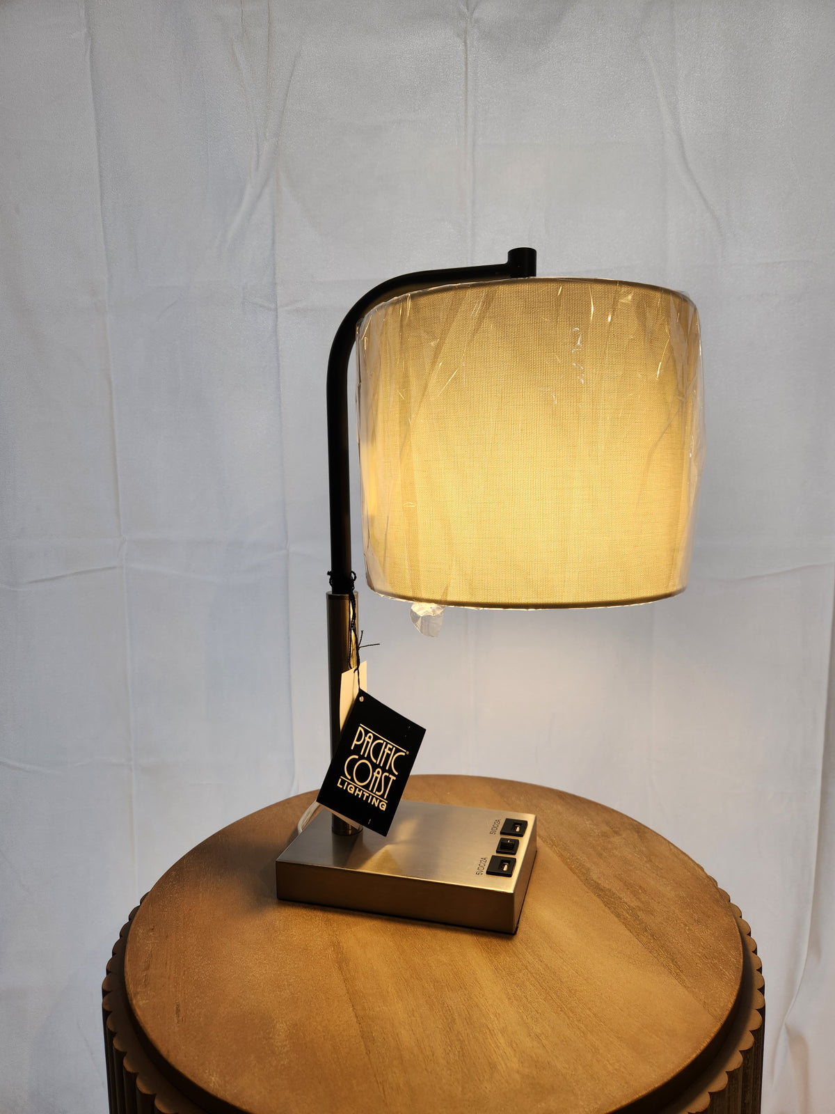The 902c0 Elton Table Lamp by Pacific Coast, with a linen shade and black frame, sits on the wooden table.