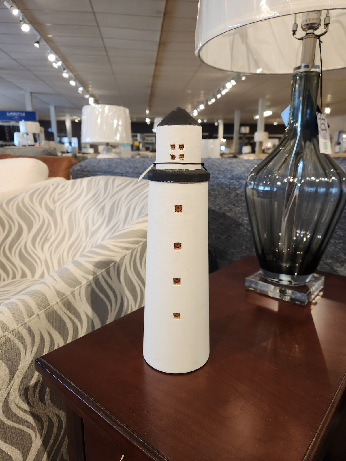 The Mercana 68795 Lighthouse (Large), a white decor piece, is displayed on a wooden table in the showroom.