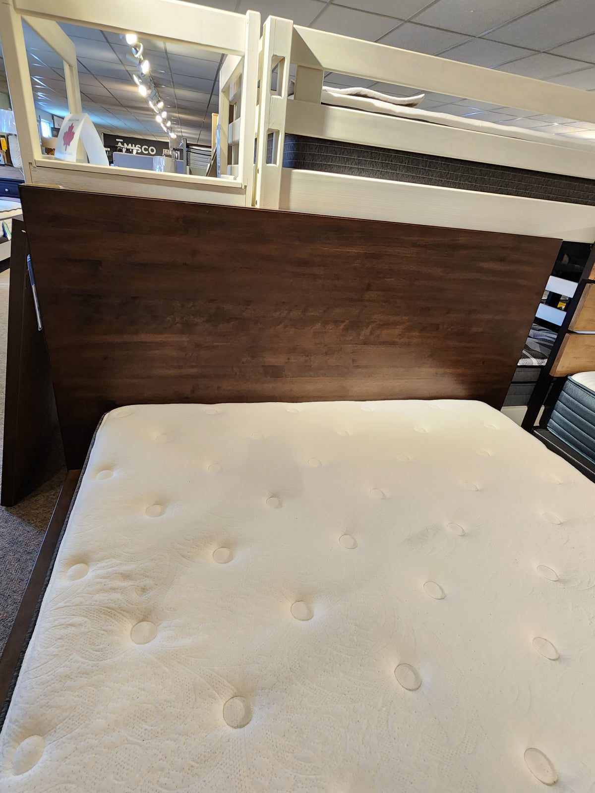 The Universal M2015 Queen Bed Frame features a white tufted mattress and dark wood headboard on display in-store.