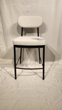 The Orly Counter Height Bar Stool by Amisco features a light gray upholstered seat and antiqued black legs on a white background.