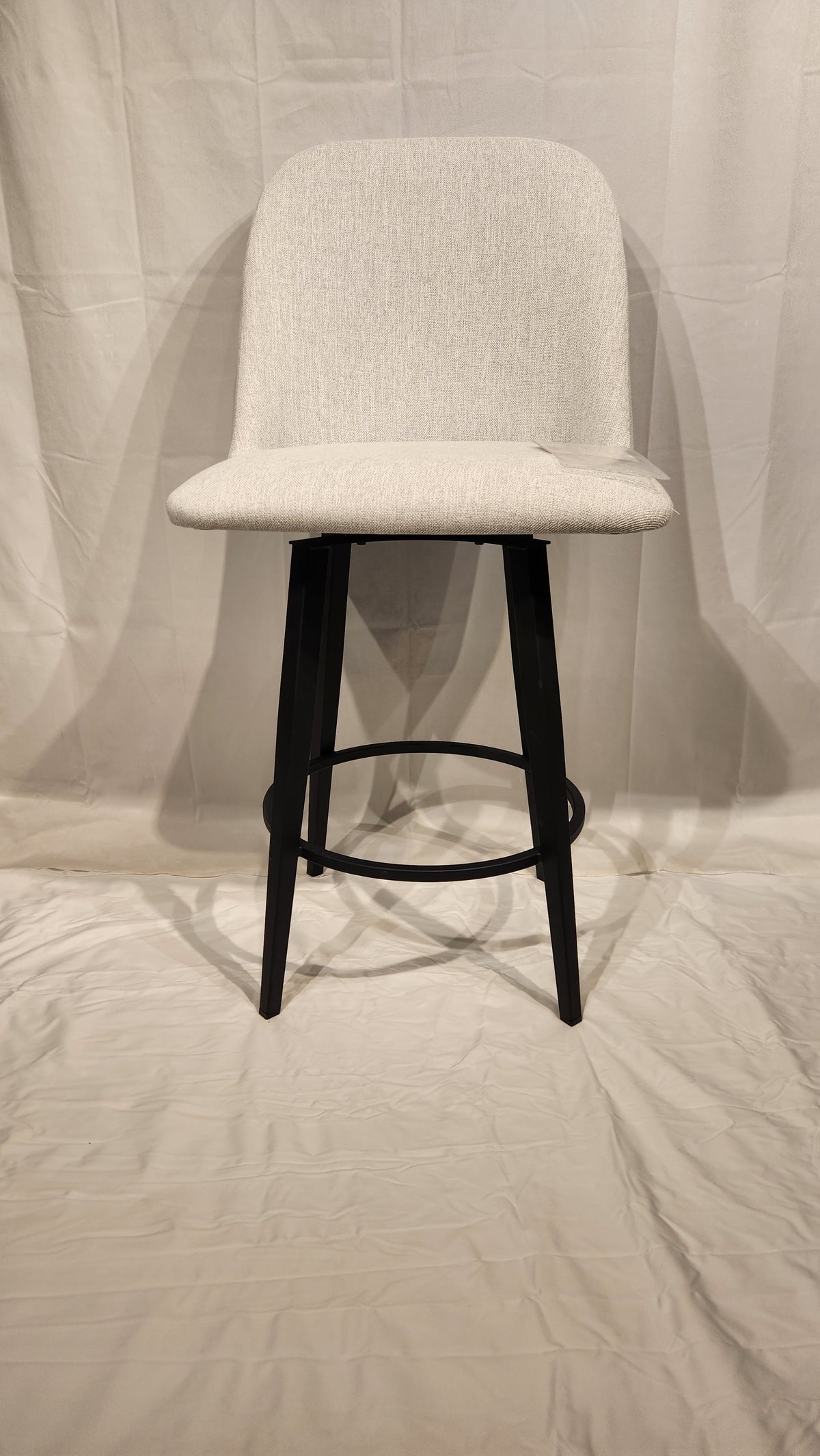 A Zahra Counter Height Swivel Bar Stool by Amisco, in light gray with curved backrest and black metal legs, on a white backdrop.
