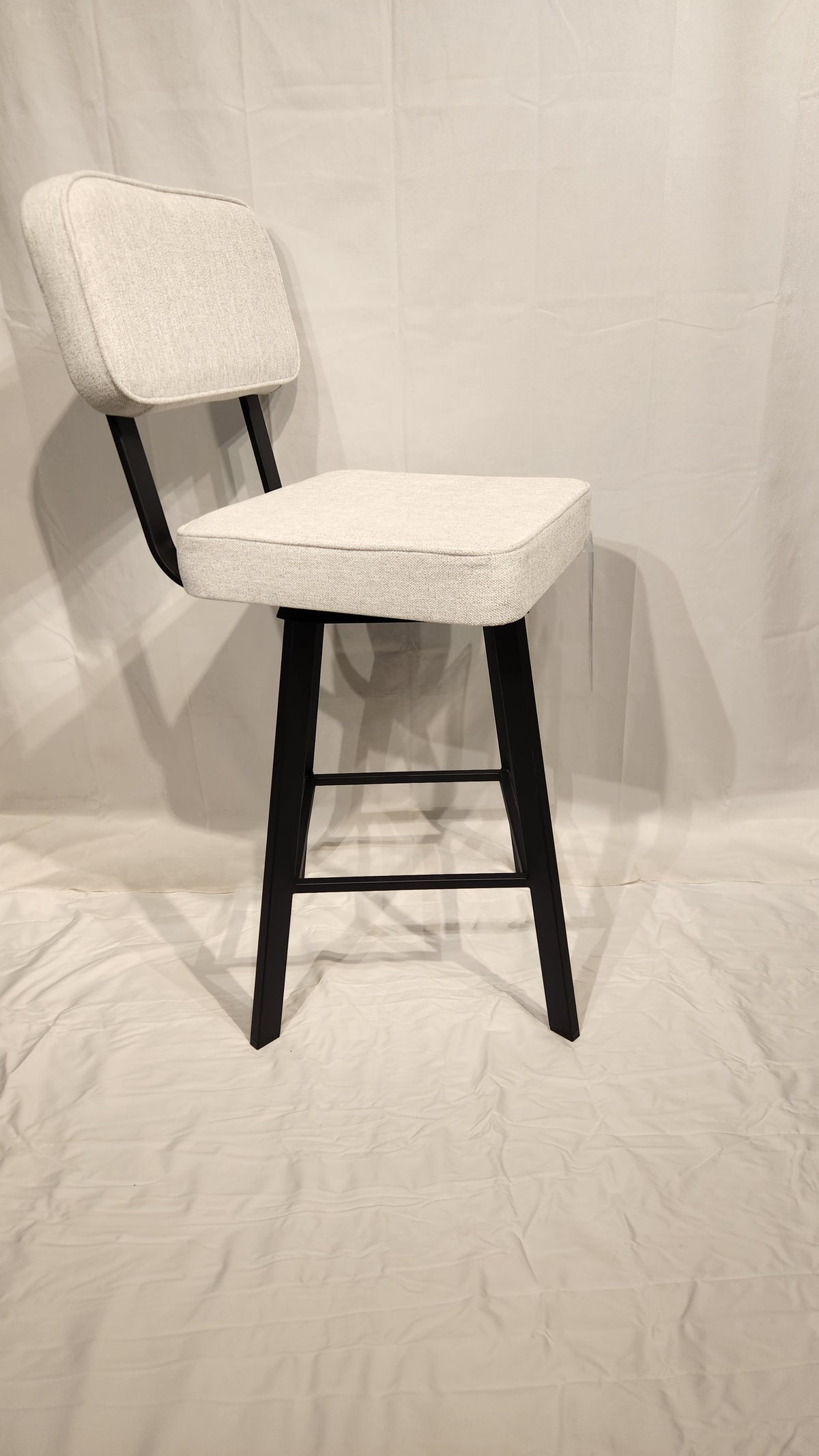 The Brixton Counter Height Swivel Bar Stool by Amisco is elegantly set on a white fabric backdrop.