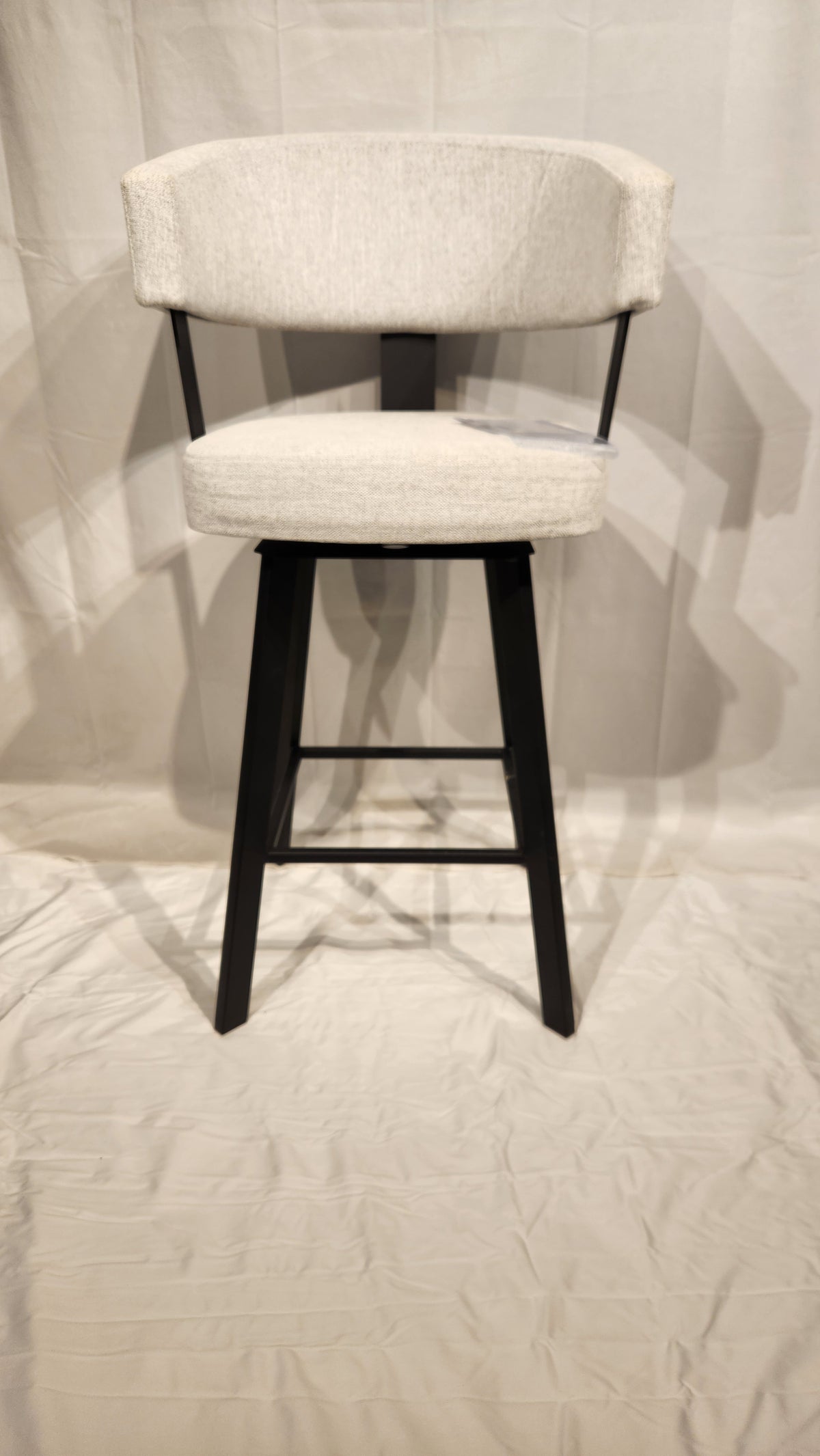 The Amisco Grissom Counter Height Swivel Bar Stool has a light gray curved backrest and black legs on a white background.