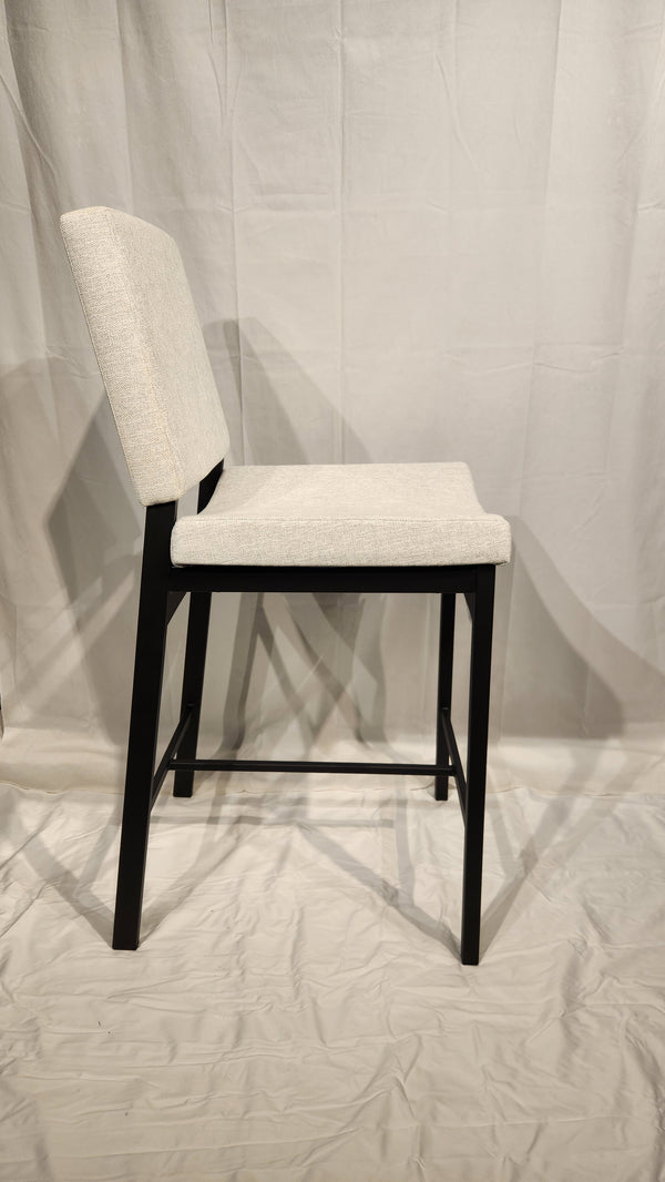 Side view of an Amisco Kendra Counter Height Bar Stool with a light beige seat and backrest, featuring black wooden legs.