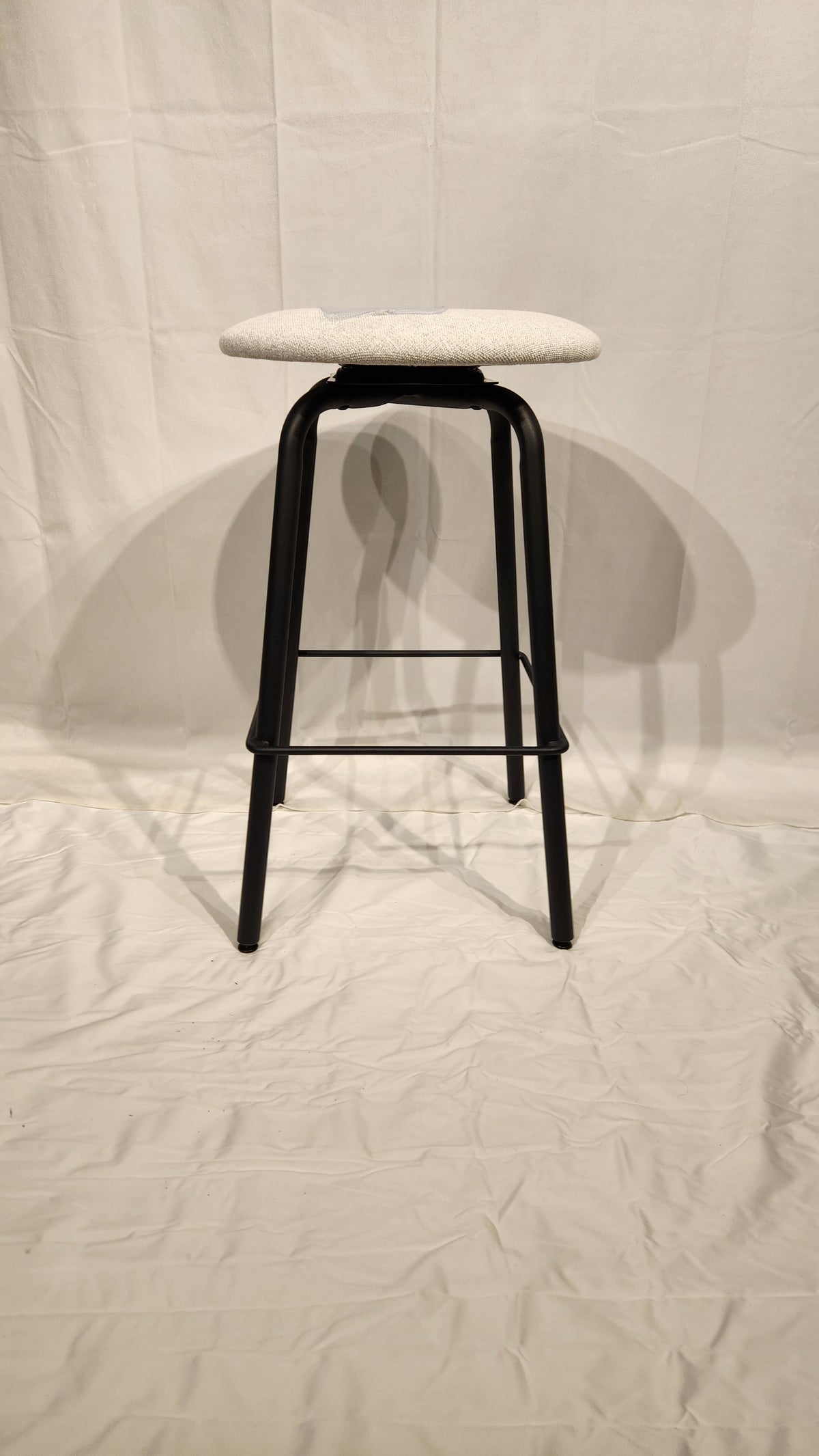 The Amisco Button Counter Height Swivel Stool features a light round seat and black metal legs on a plain white backdrop.