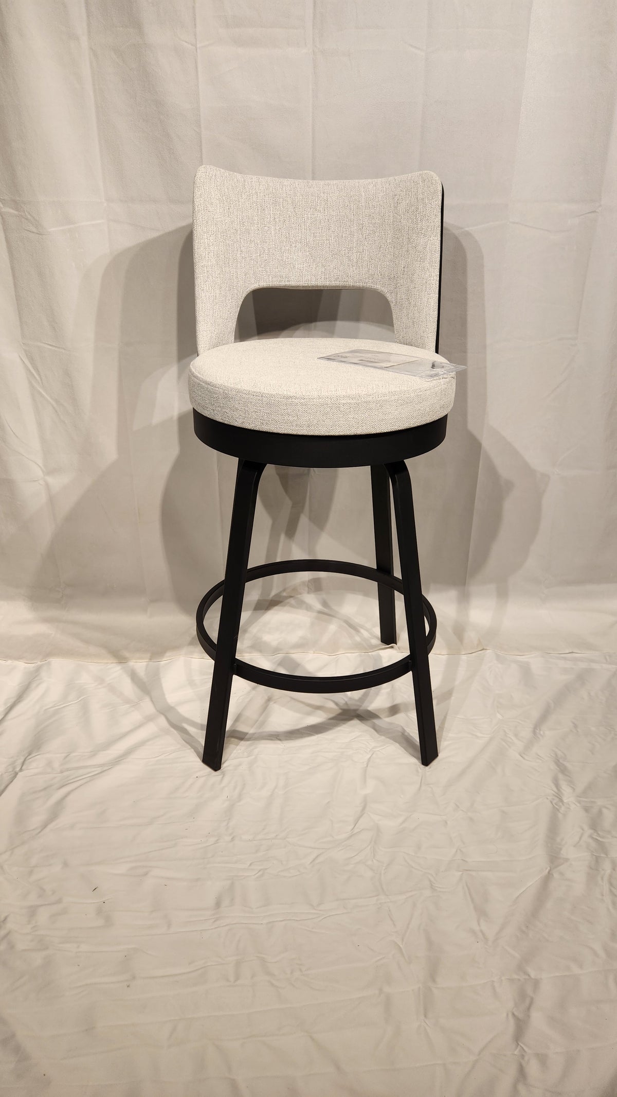 The Amisco Brock Counter Height Swivel Bar Stool features a light gray padded seat, black frame, and circular footrest.