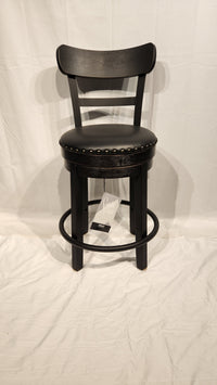 An Ashley Valebeck D546 black wood bar stool features a cushioned round seat, metal footrest, and nailhead trim.