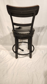 The Valebeck D546 bar stool by Ashley is black faux leather with a cushioned seat, metal footrest, and backrest.