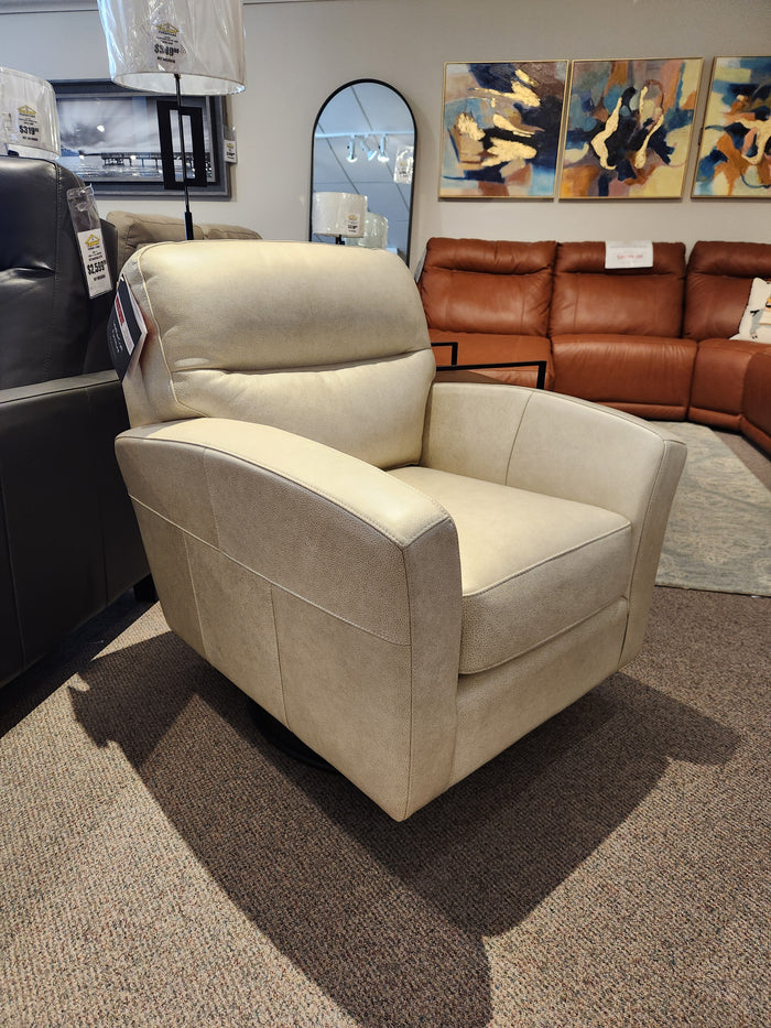 The Leather Craft 744 Leather Swivel Chair in beige is shown in a showroom with sofas and artwork behind it.