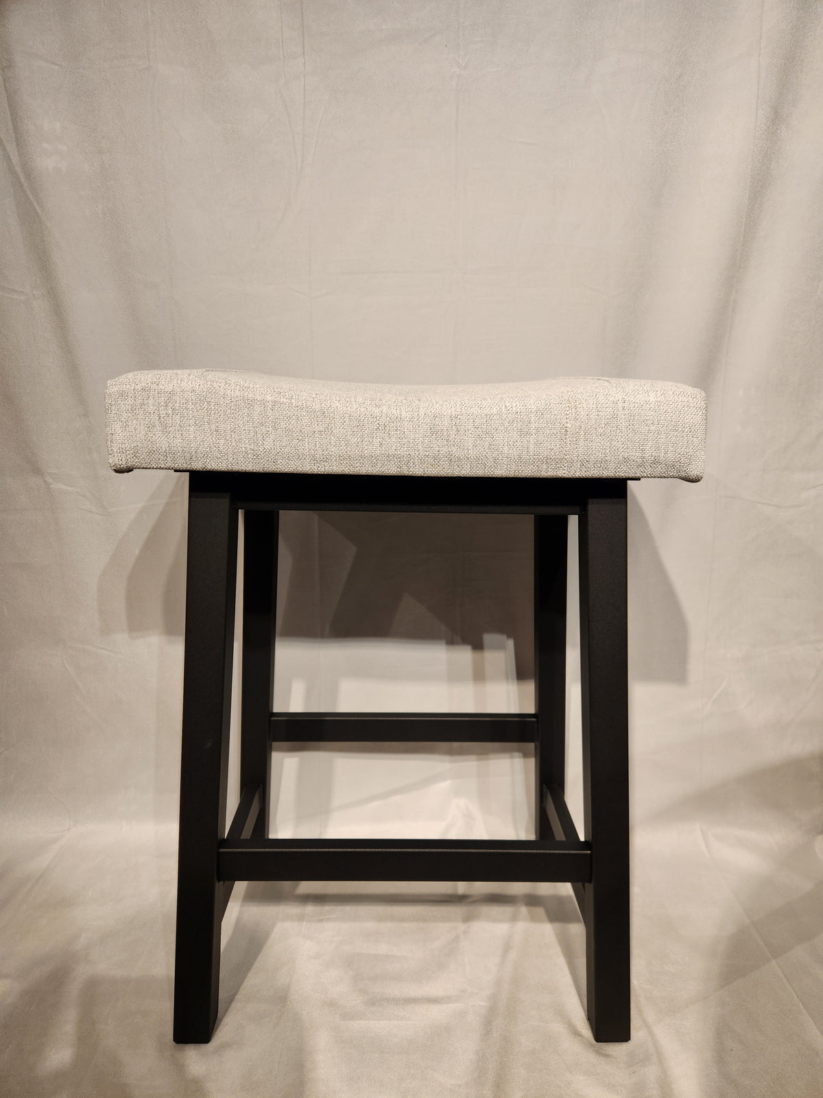 The Amisco Miller Counter Height Bar Stool features a light gray cushion and black wooden legs against a neutral backdrop.