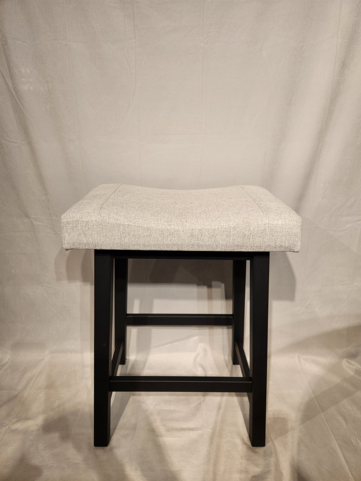The Amisco Miller Counter Height Bar Stool features a light gray cushioned seat and black wooden legs.