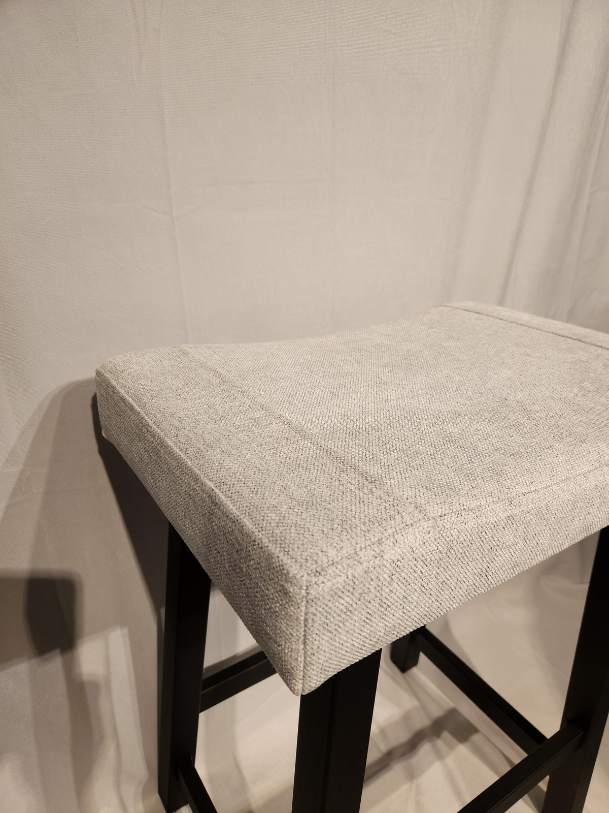 The Amisco Miller Counter Height Bar Stool features light gray upholstery and a black metal frame against a light backdrop.