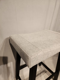 The Amisco Miller Counter Height Bar Stool features light gray upholstery and a black metal frame against a light backdrop.