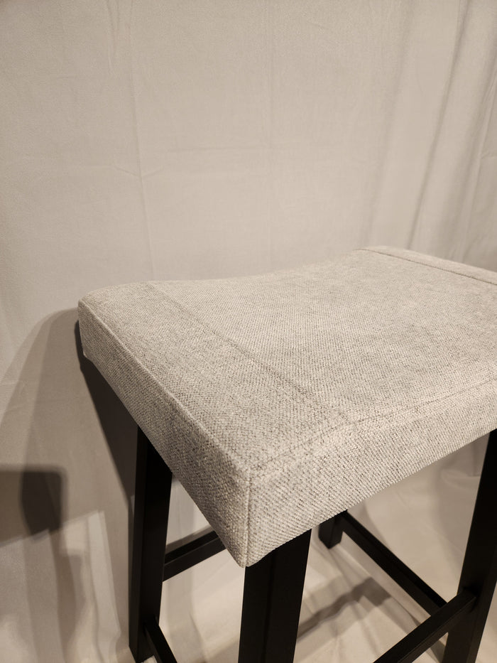 The Amisco Miller Counter Height Bar Stool features light gray upholstery and a black metal frame against a light backdrop.