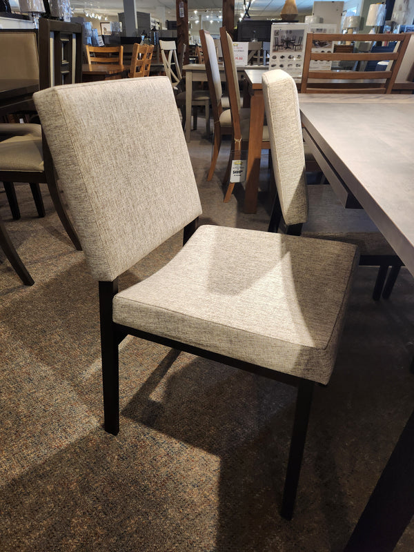 A beige dining chair with dark wooden legs beside the Amisco Lewis 36"X48" Table Package in a modern showroom.