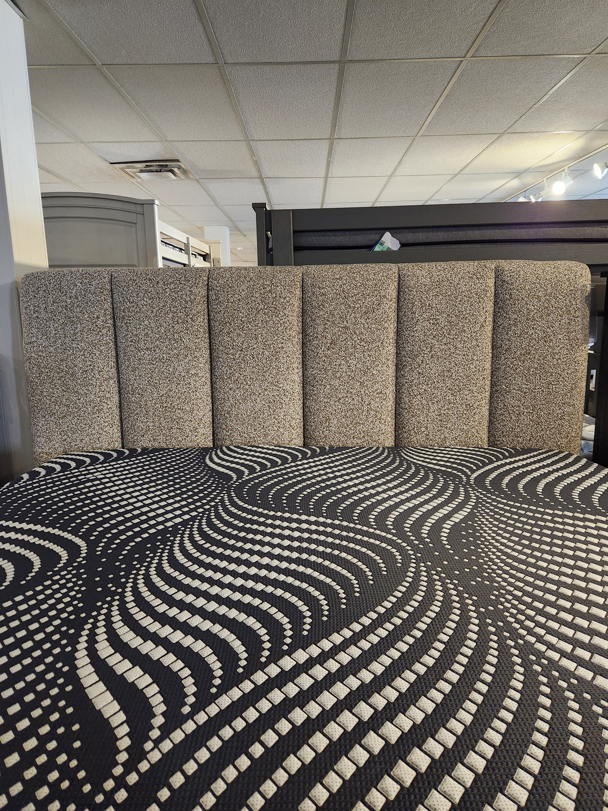 Palliser's Verttia 77140 King Bed, power-adjustable with a textured headboard, black and white bedspread, in grid-ceiling room.