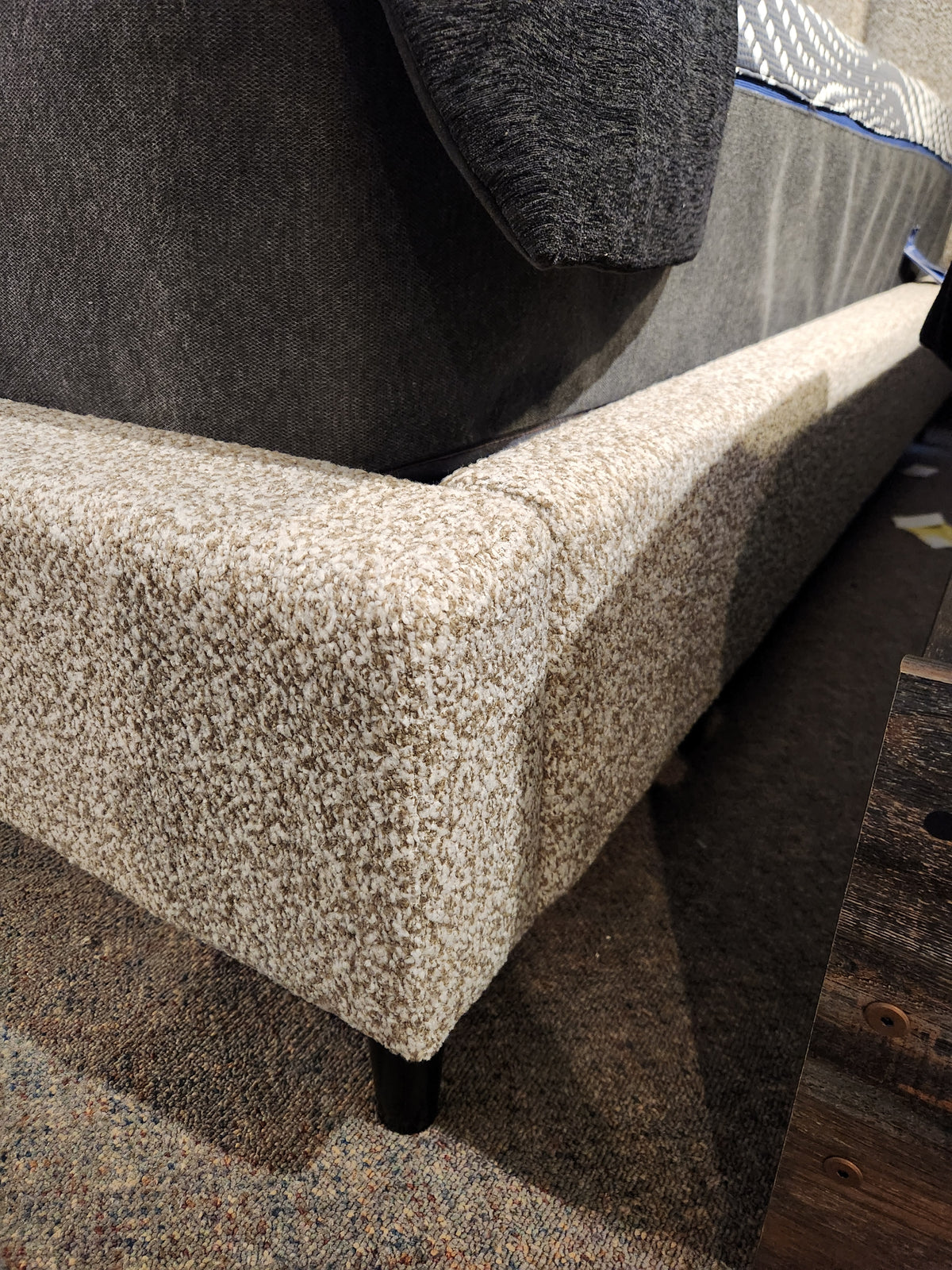 Close-up of Palliser's Verttia Power-Adjustable Bed with beige fabric and dark legs, near wood, highlighting adjustability.