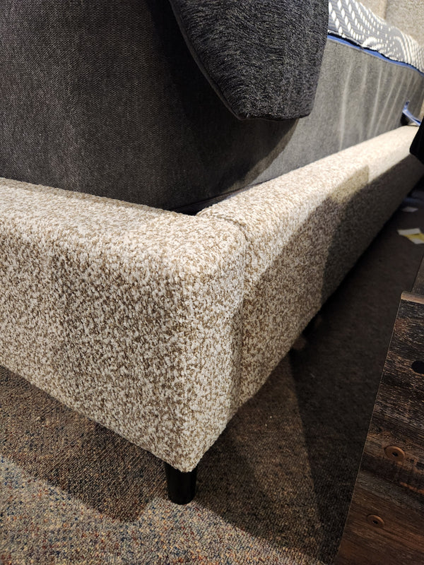 Close-up of Palliser's Verttia Power-Adjustable Bed with beige fabric and dark legs, near wood, highlighting adjustability.