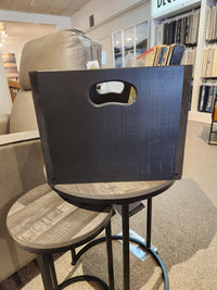 The SB101 Record Crate by Mercana is on a round side table near a gray armchair in a showroom with fabric displays.