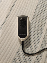 A Tempur-pedic Lift 2.0 Adjustable Base remote with Head Lift rests on a textured fabric surface.