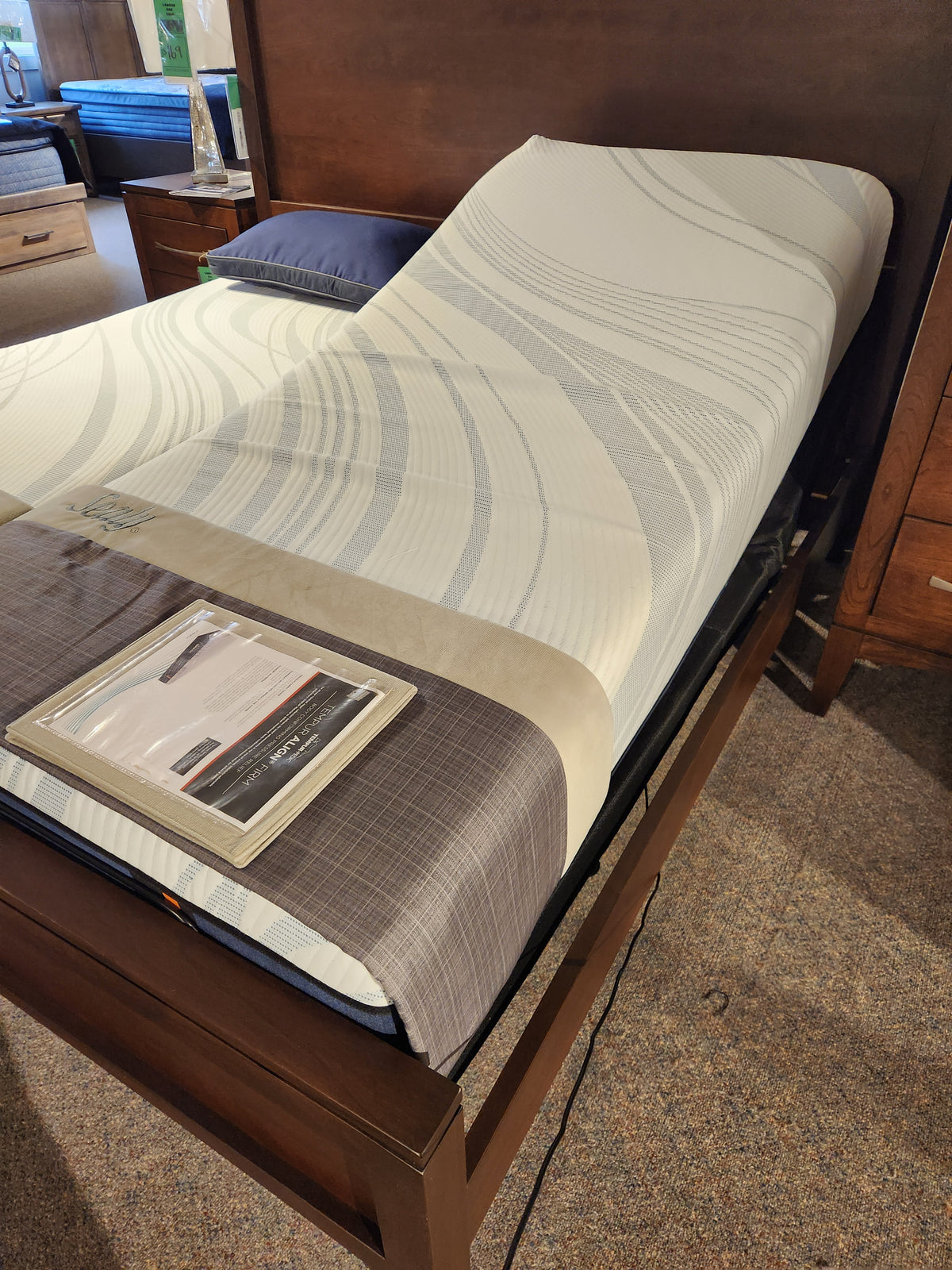 Tempur-pedic Lift 2.0 Adjustable Base with head lift and wood frame shown in showroom with informational pamphlet.