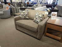 The Simmons Upholstery 1014 Trinity Chair Bed in beige, with two patterned pillows, is shown next to a wooden side table.
