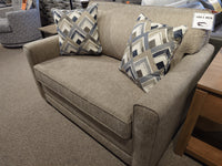 Simmons Upholstery 1014 Trinity Chair Bed in beige with two geometric pillows, shown in a furniture showroom.