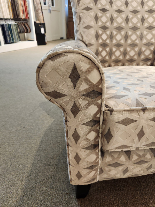 Close-up of Decor-rest's 2470 Stationary Accent Chair, a Canadian-made upholstered armchair featuring a geometric pattern in neutral colors. It is elegantly placed on a carpeted floor in the Decorest showroom, exemplifying contemporary design and craftsmanship.