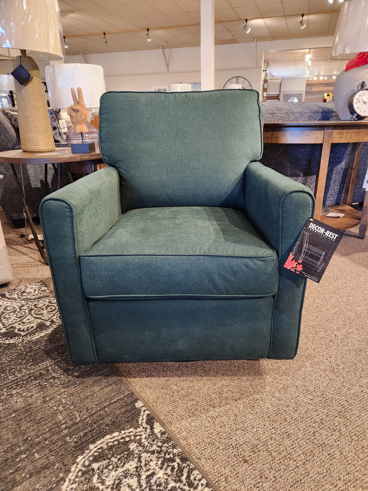 The 2284 Swivel Accent Chair by Decor-rest, featuring a green upholstery and optimal support with a rectangular backrest, is displayed on a carpeted floor in a furniture store.